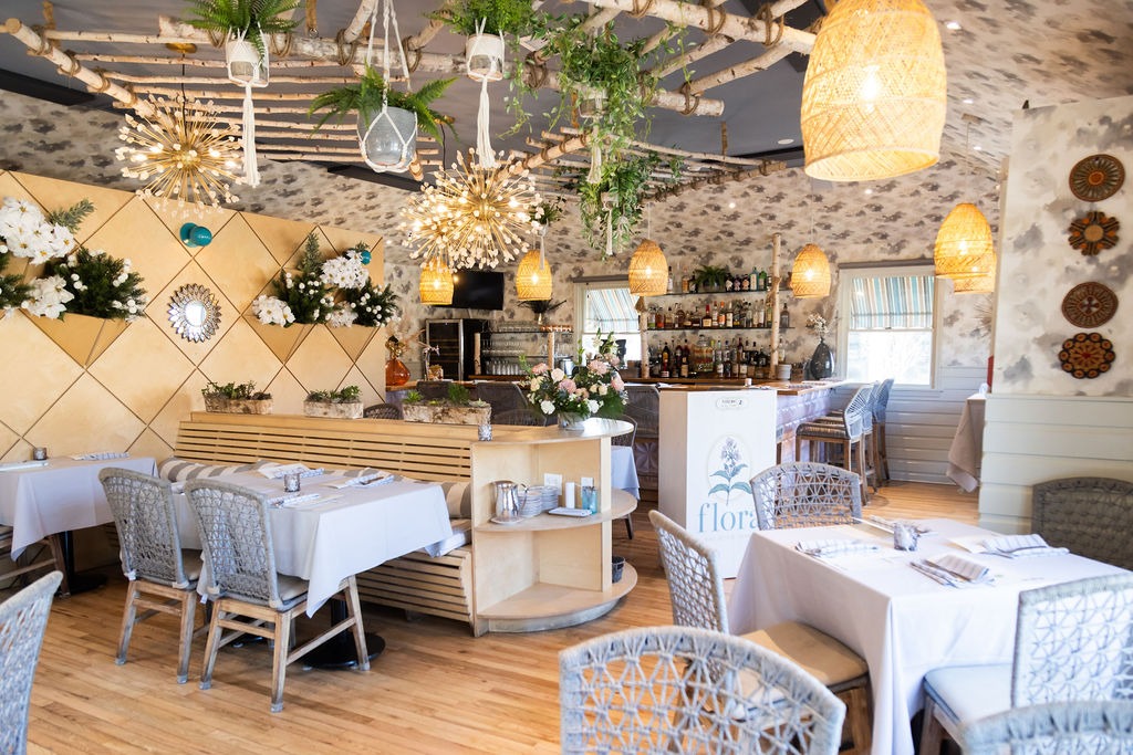 Floral restaurant interior with tables, chairs, bar, and hanging plants.