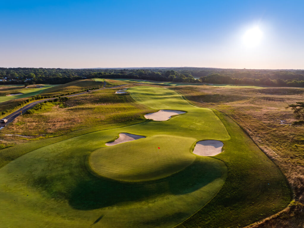 Aerial view of a golf course with sand traps and a red flag on the green.