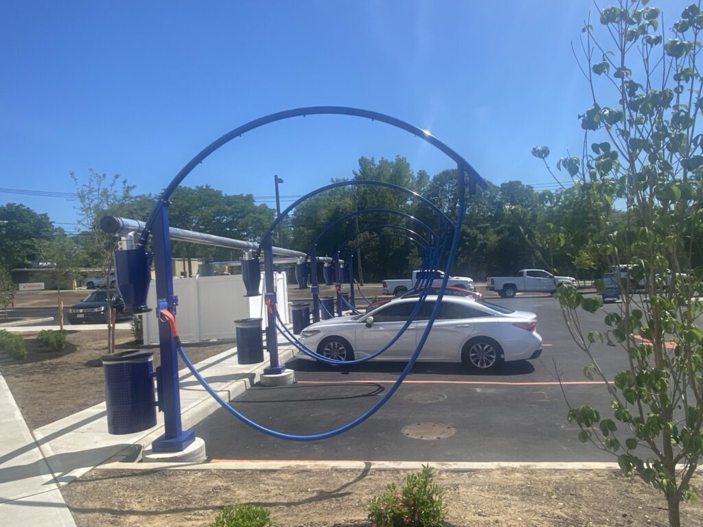 A white car is at a car wash with blue arches and equipment.