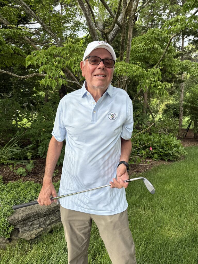 Man in a light blue striped polo and white cap holds a golf club.