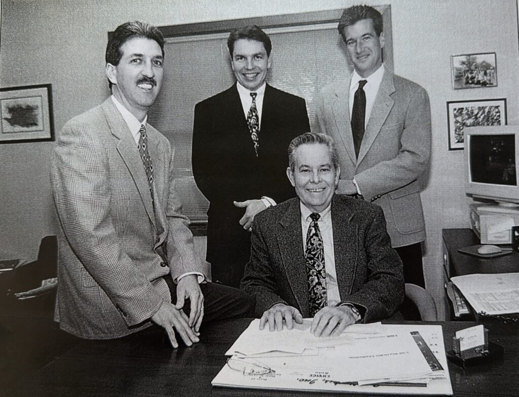 Four men in suits pose in an office.