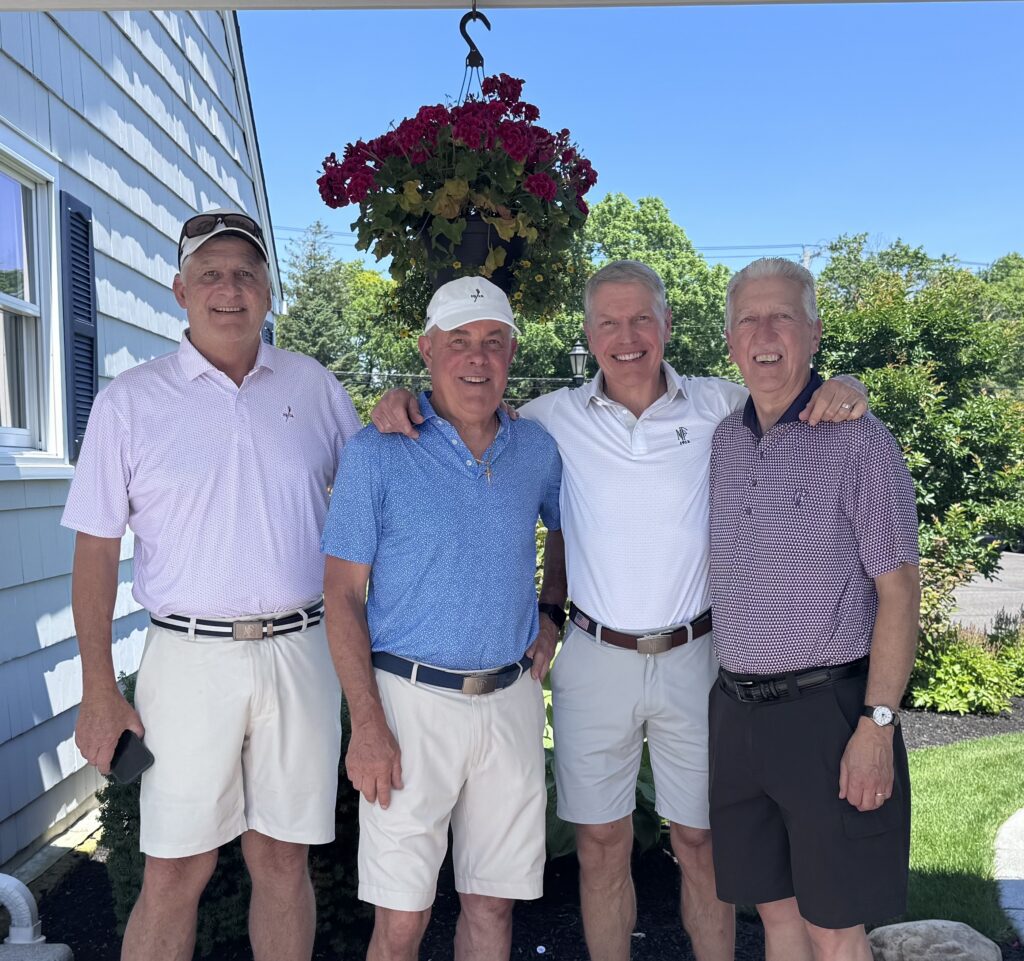 Four men in golf attire pose for a photo outdoors.