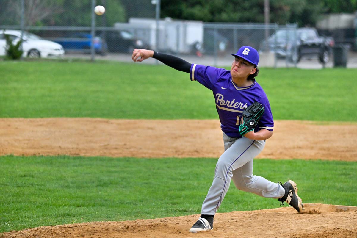 A baseball pitcher in a purple jersey and gray pants pitches the ball.