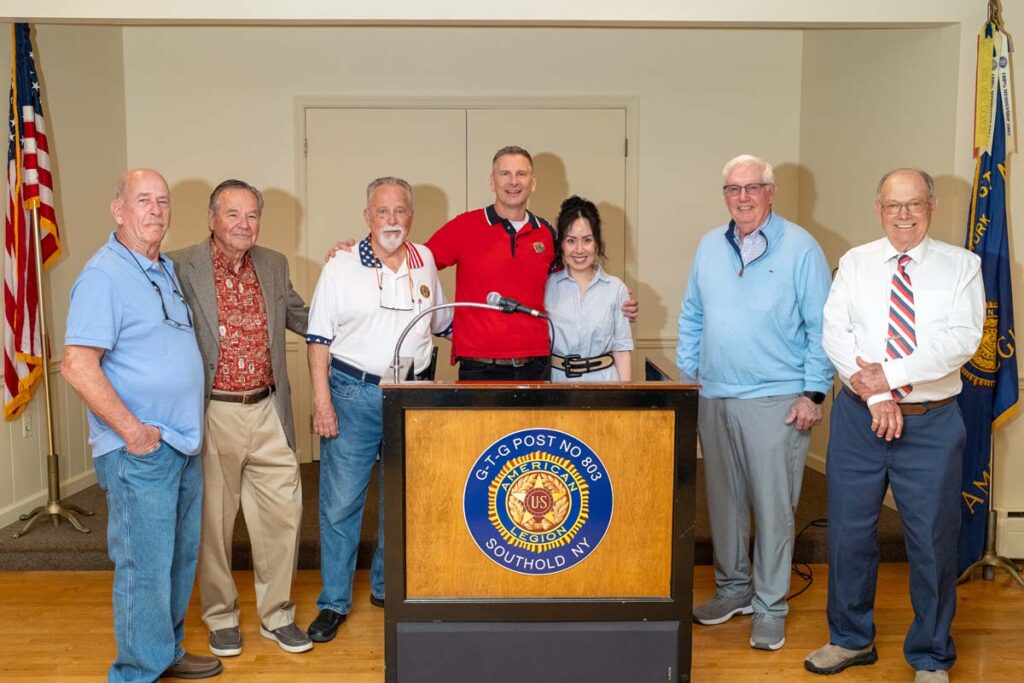 Six white men and a white woman stand in a line, three of them behind a podium.