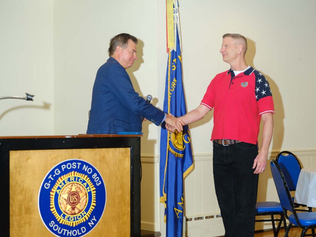 Two white men shake hands. One holds a microphone in his hand.