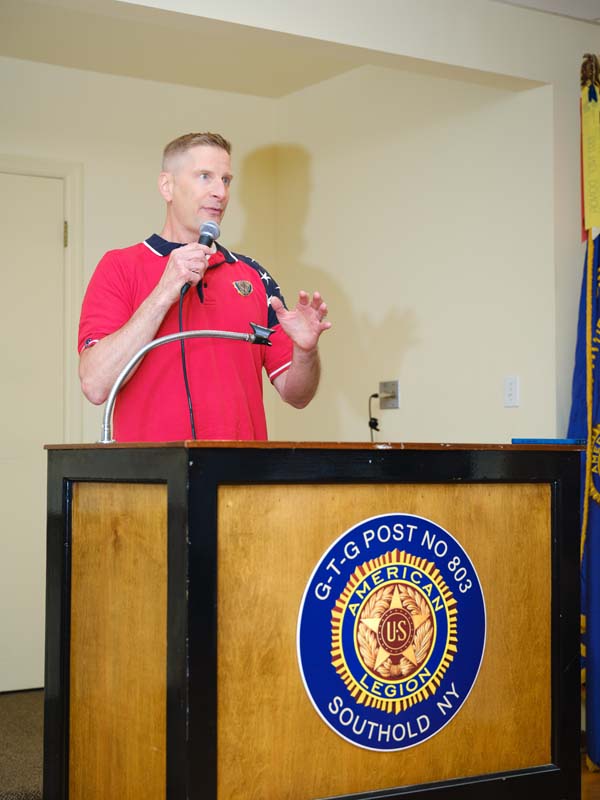 A white man stands behind a podium and speaks into a microphone in his hand.