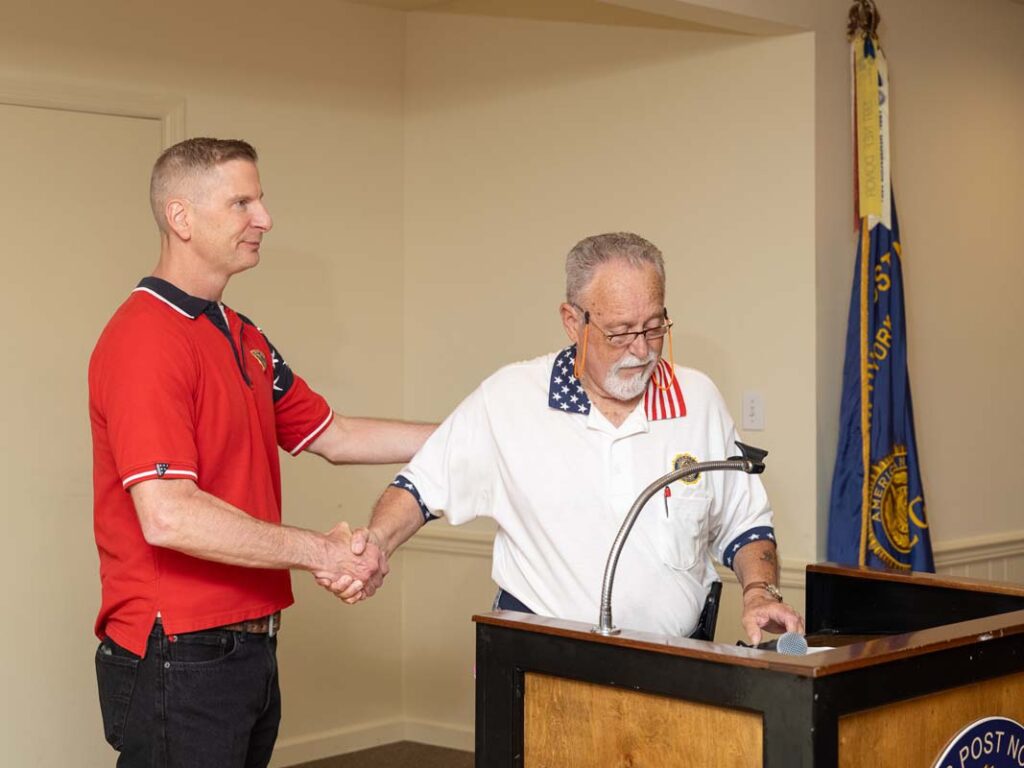 Two white men shake hands. Their shirts have stars and stripes, referencing the American flag on them.