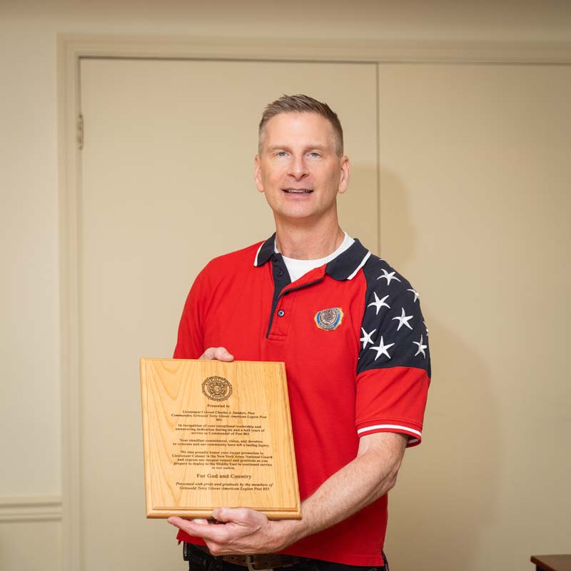 A white man holds a wooden plaque he received.