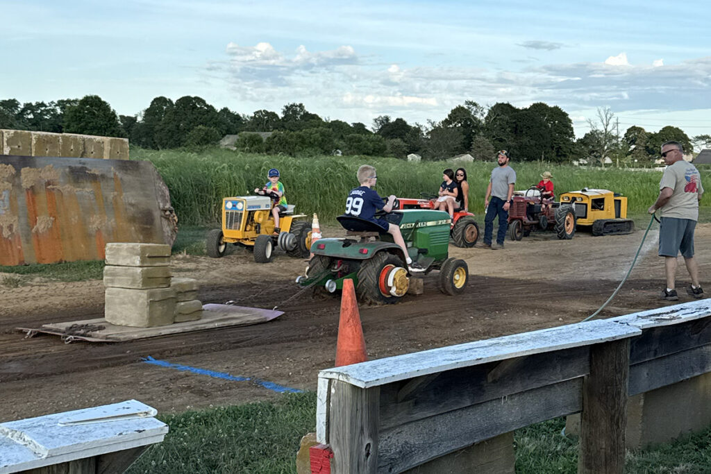 A boy in a blue t shirt drives a green garden tractor with over a thousand pounds on the sled.