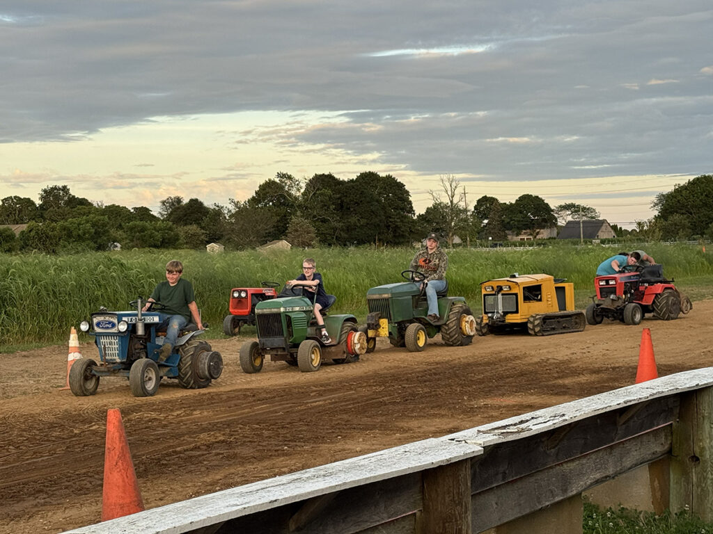 Five garden tractors are in a line with junior tractor pullers waiting their turn at the sled