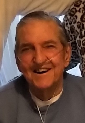 An elderly man wearing a breath apparatus and a grey long-sleeved shirt smiles at the camera.