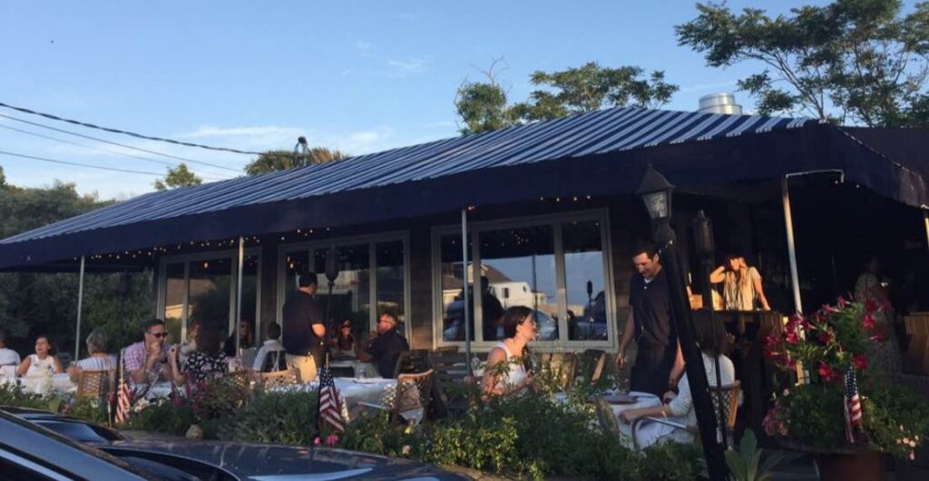 Outdoor dining at a restaurant with blue and white striped awning and people seated at tables.