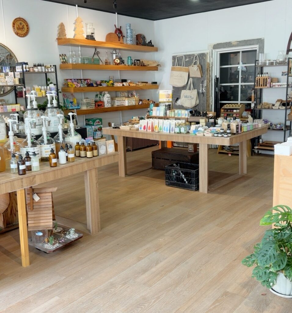 A retail store displays various products on shelves and tables, including soaps, lotions, and bags.